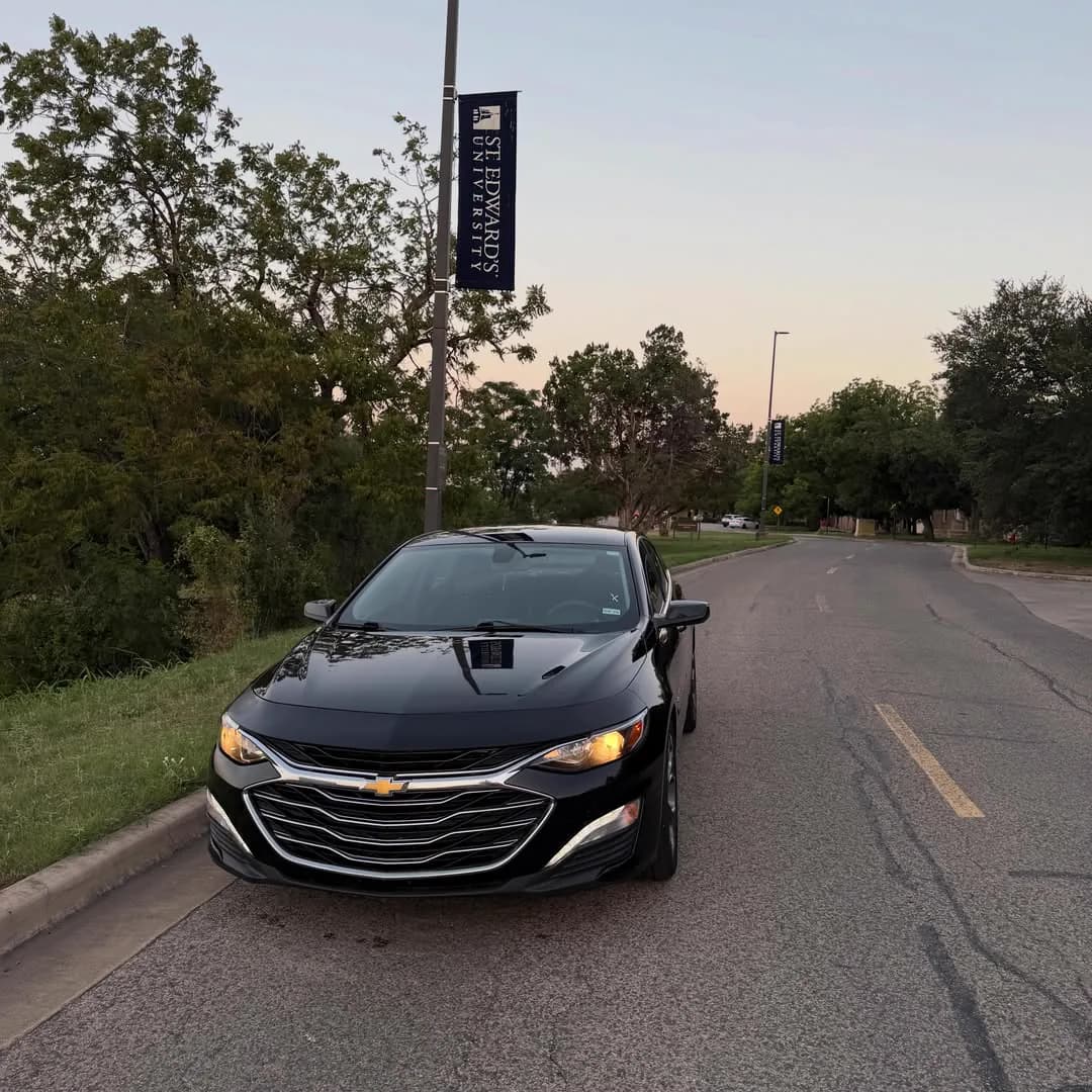 The black Chevrolet Malibu photographed head-on, parked on a tree-lined street.