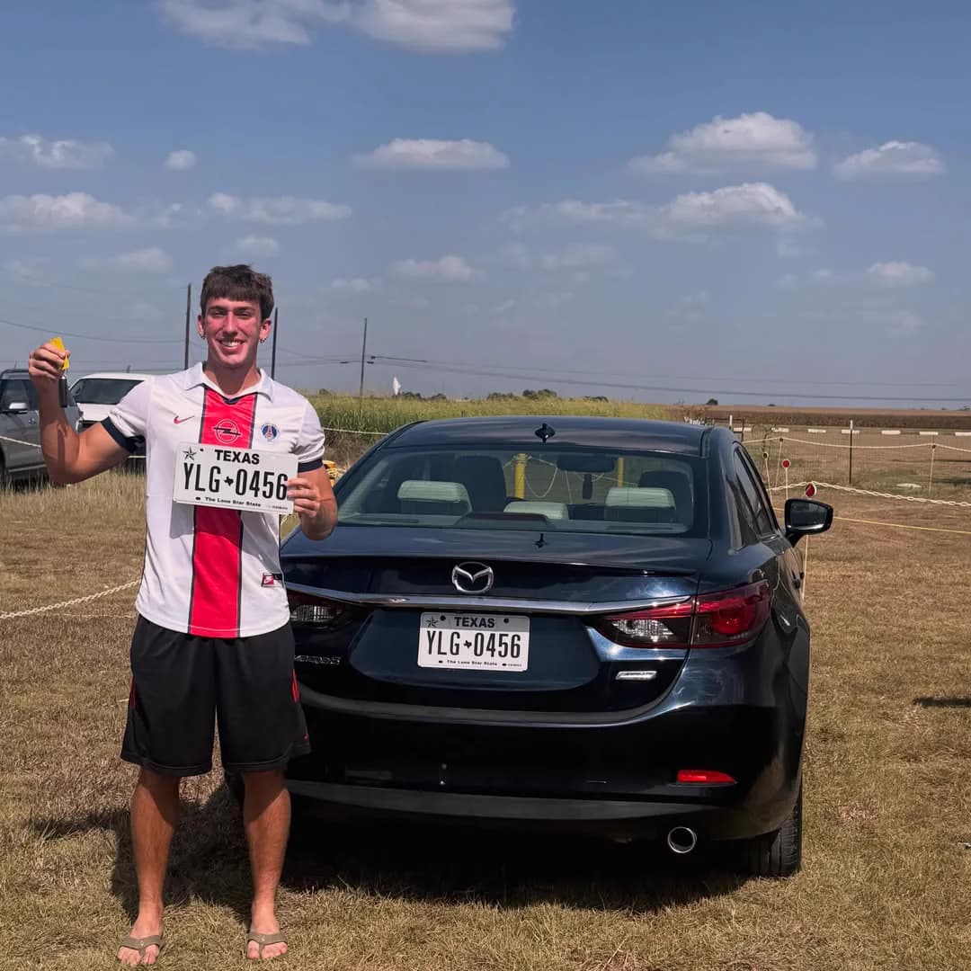 A customer holding up the new licence plate behind the dark blue Mazda 6 he bought.