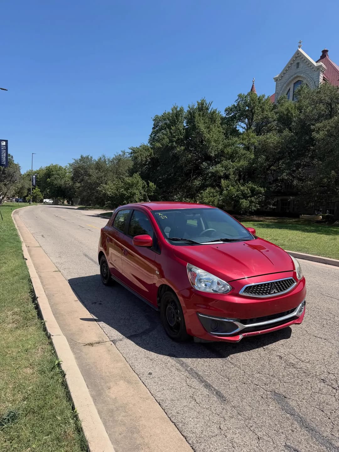 The red Mitsubishi Mirage hatchback parked at the kerb on a bright afternoon.